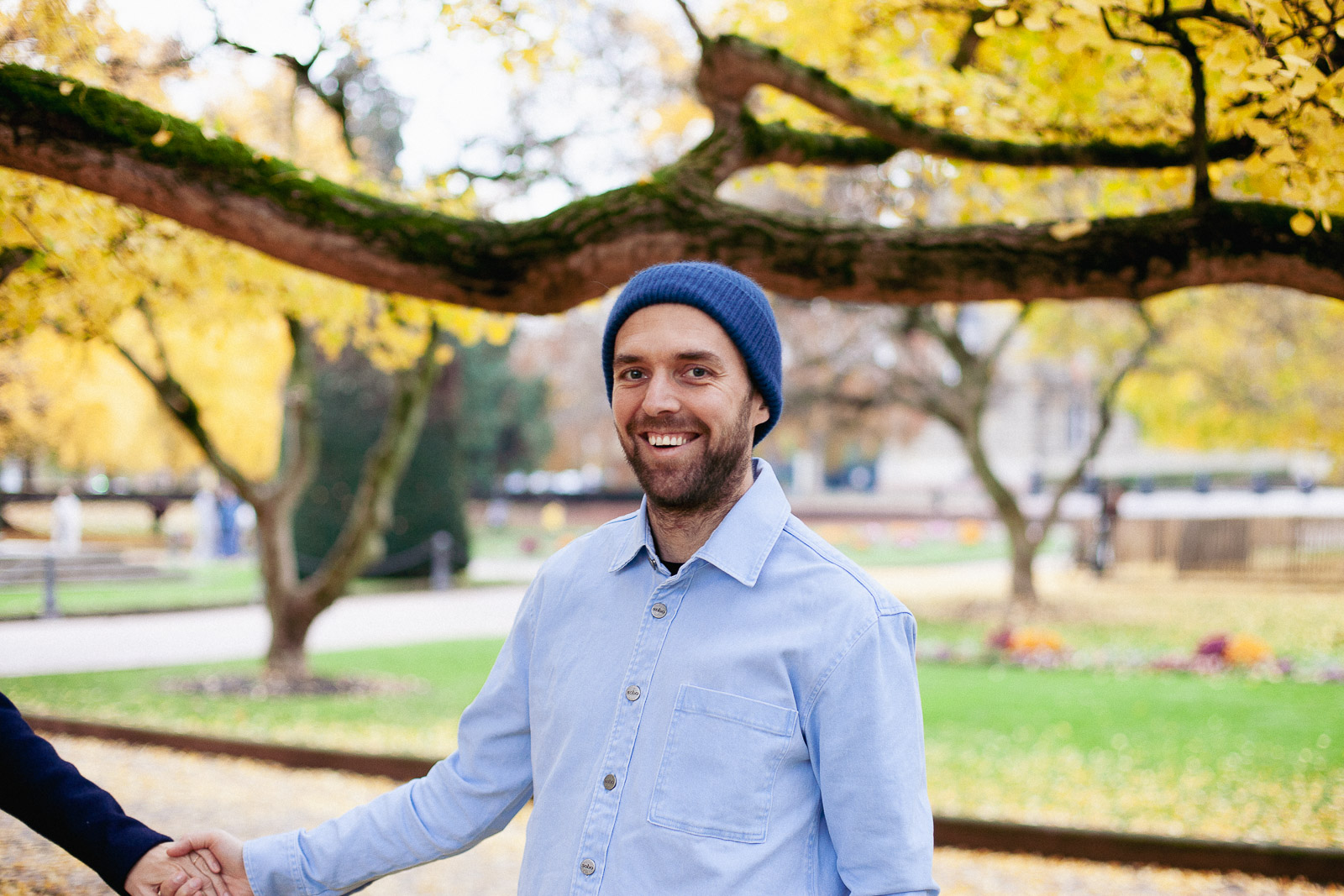 Tanguy lance un sourire à la caméra devant un arrière-plan aux couleurs automnales